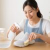白いメッシュ素材のスニーカーを手にした日本人女性が、洗面台で漂白前の状態を確認している様子を写した清潔感のある写真。漂白作業の雰囲気が自然に伝わる構図。